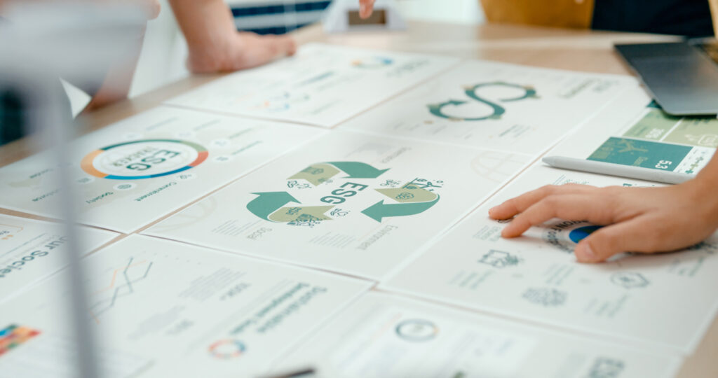 Closeup of team members examining ESG-related documents, pointing and discussing investment strategies for sustainable and renewable energy resources during an eco-friendly business meeting.