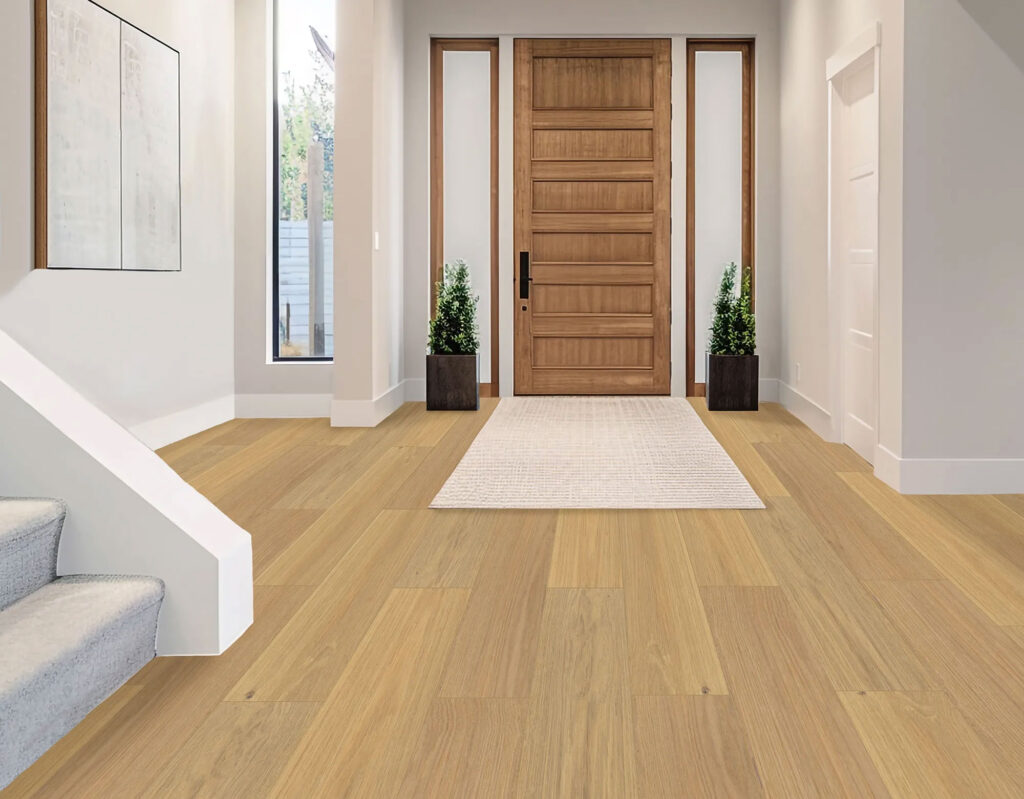 A modern entryway featuring Aristo-Ash light wood flooring, a wooden front door, white walls, a beige runner rug, gray carpeted stairs, and two potted plants near the entrance.