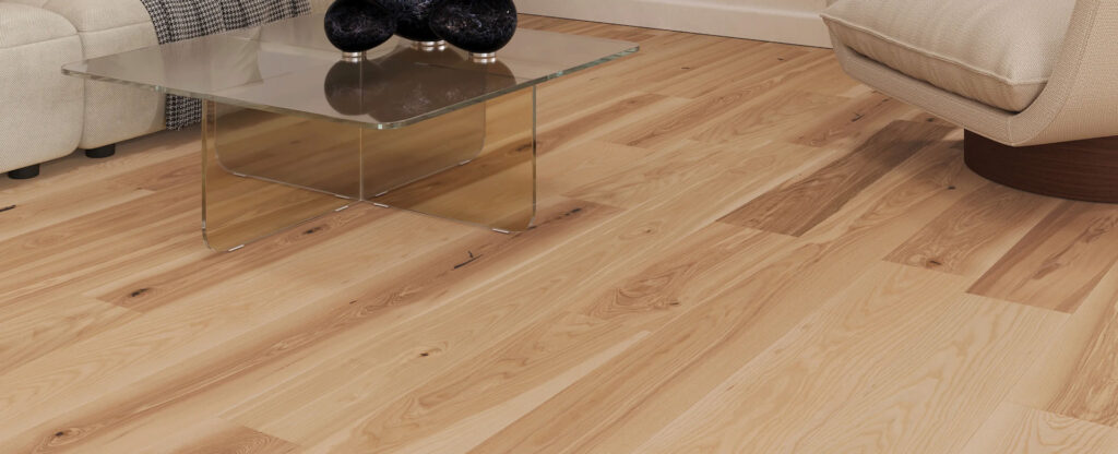 Coastal-Sands light hardwood flooring with visible knots and grain shown beside a glass coffee table and the corner of a beige upholstered chair.