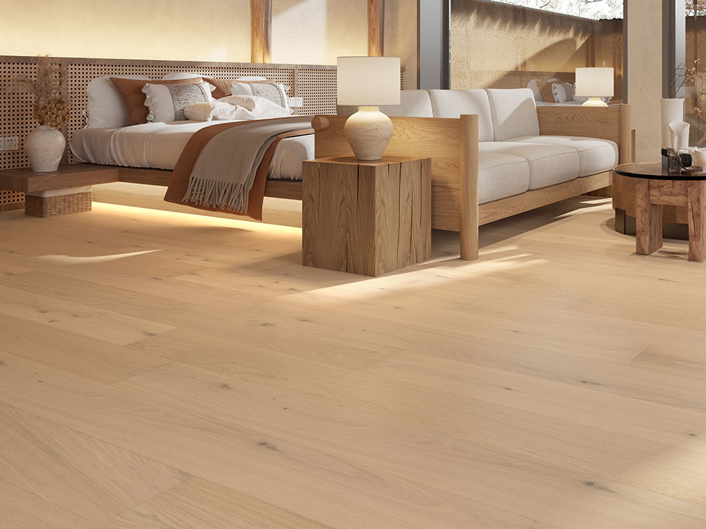 Modern bedroom featuring Aristo-Ash-web light wood flooring, a bed with white and beige bedding, a beige sofa, wooden furniture, and soft lighting.
